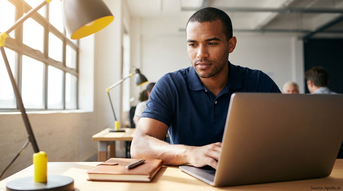 Man typing on a laptop with a notebook on a desk in a modern office.