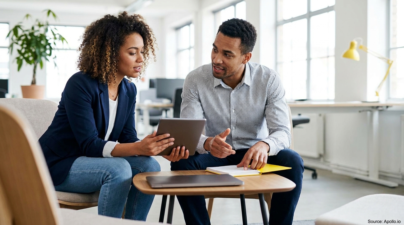 Two colleagues discuss data on a tablet and notebook in a modern office.