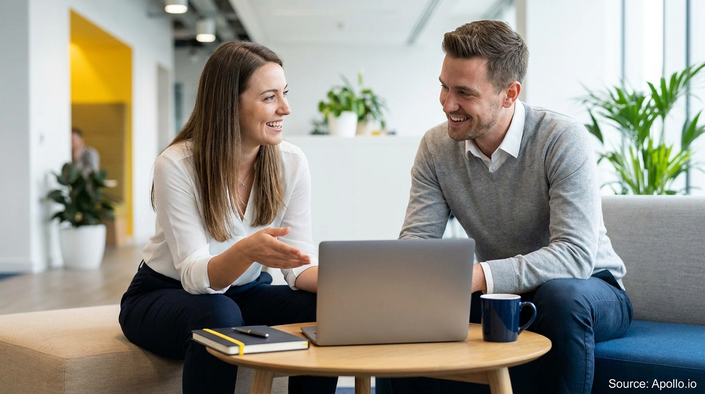 Two smiling colleagues discuss work with a laptop in a modern office.