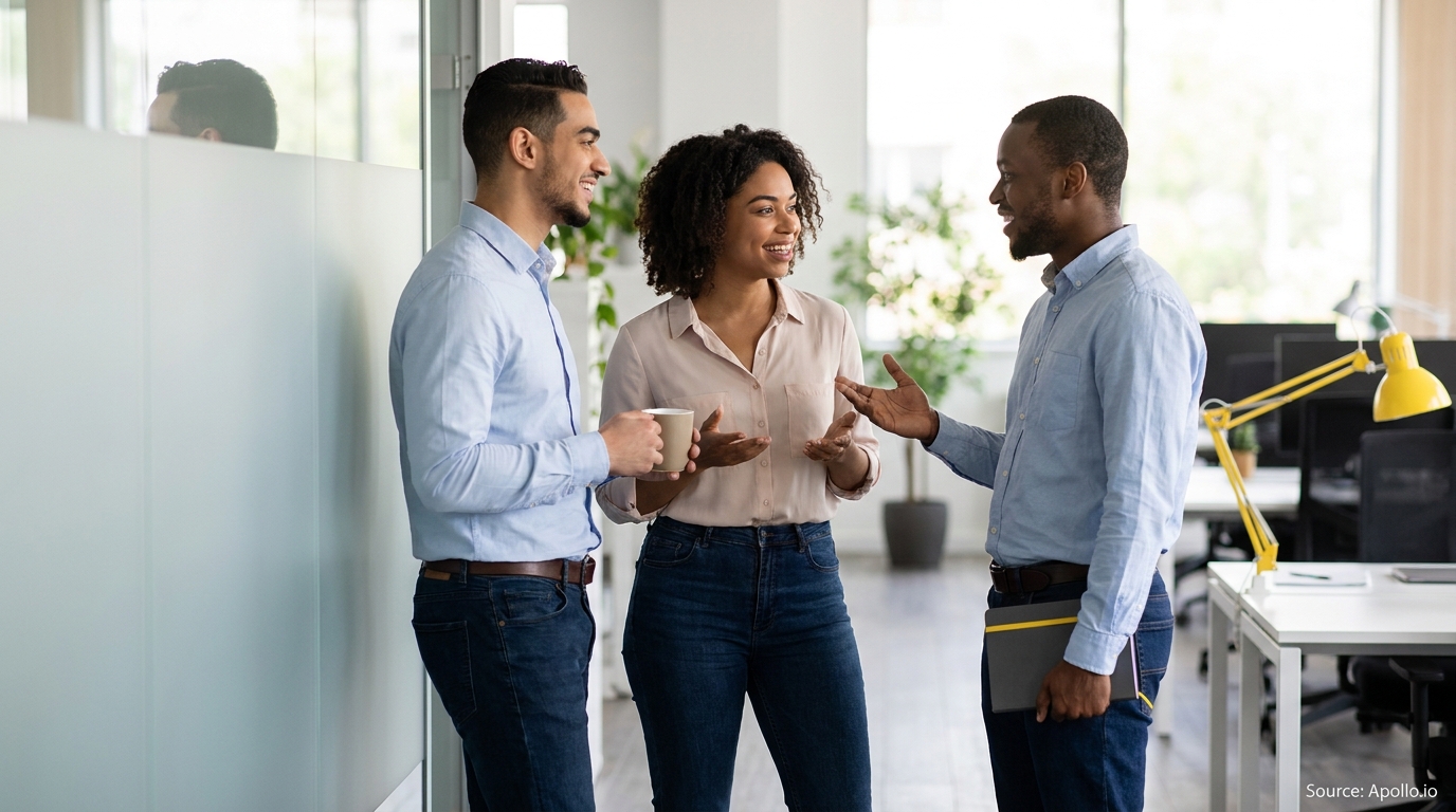 Three professionals talk and gesture in a modern office environment.