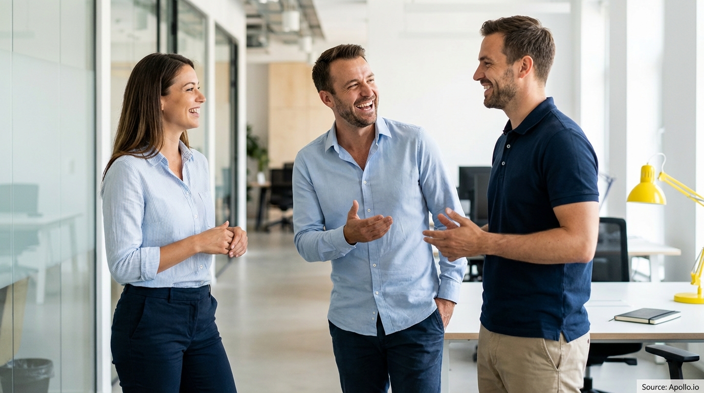 Three smiling colleagues talk and laugh in a bright, modern office.